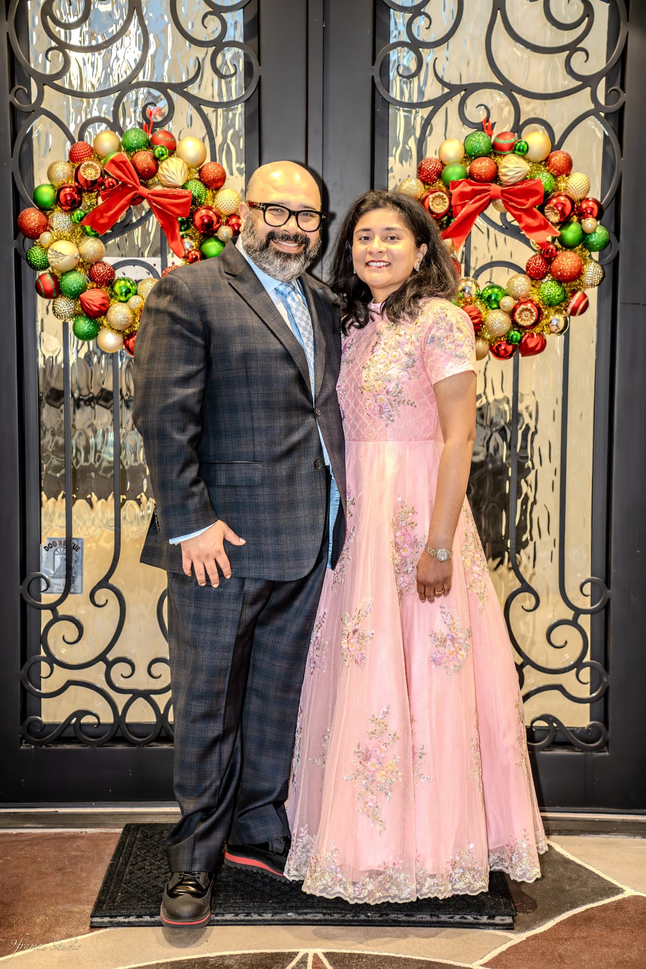 Sankha and Pallavi at the front door between two red and green holiday wreaths