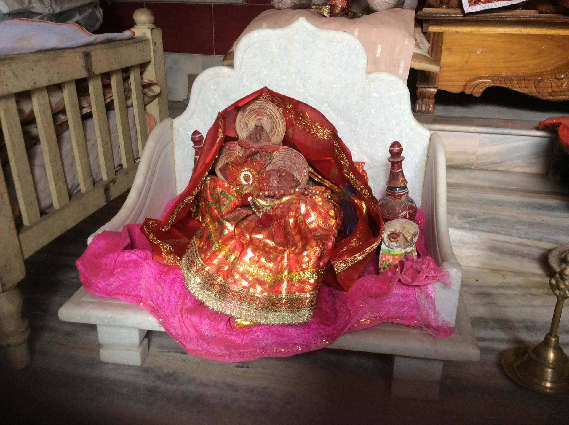 A deity dressed in red and gold cloth on a white marble seat, with a small painted owl beside her